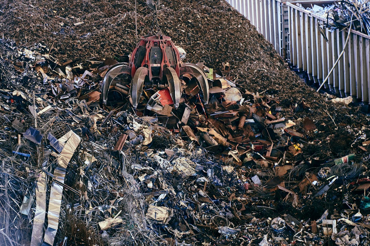 İzmir Hurdacı A claw excavator sifting through a large pile of industrial scrap metal outdoors.